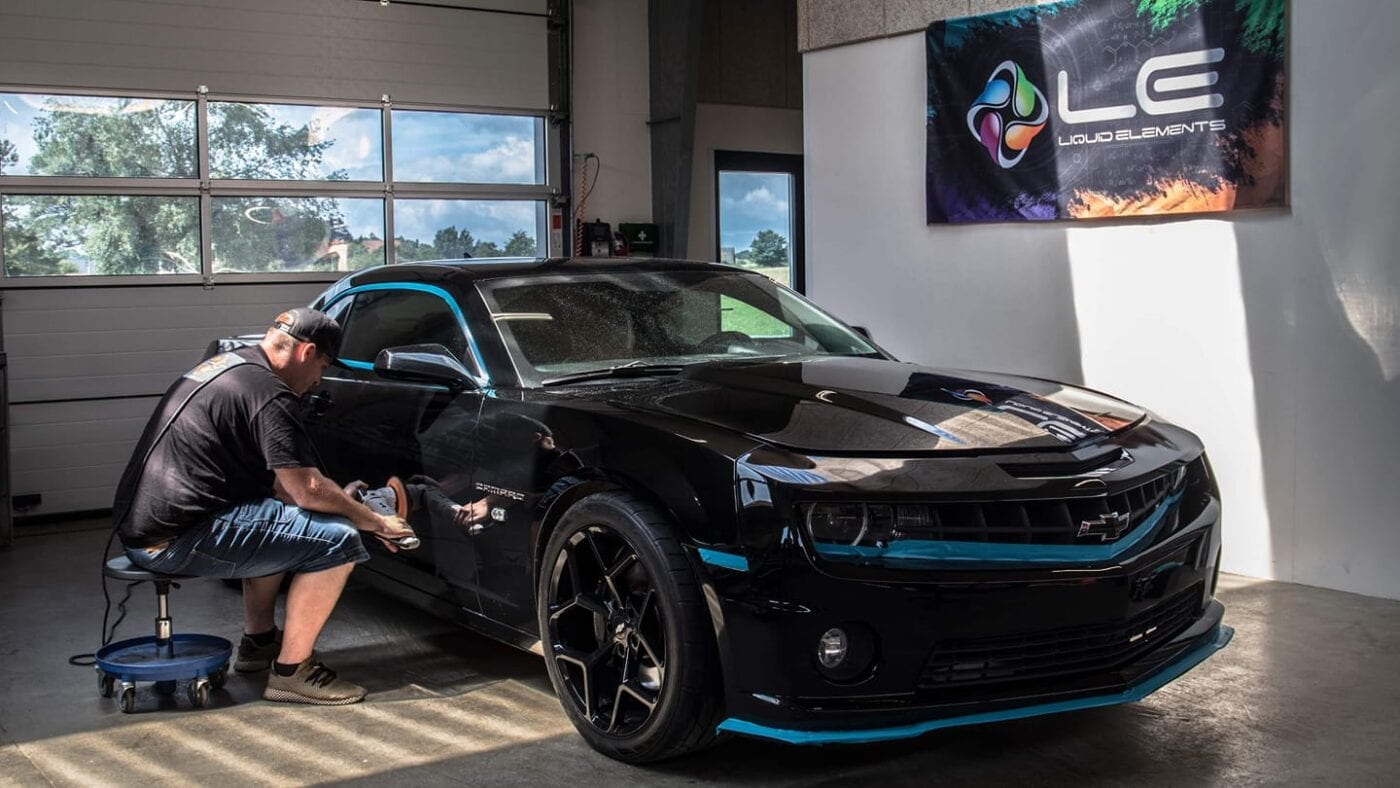 A man is working on a black and blue chevy camaro.